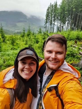 Dağların ortasında yaz mevsiminde sarı yağmurlukla selfie çeken çift yürüyüşçüler.