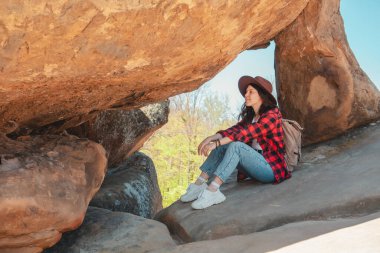Kotlu ve şapkalı mutlu kadın kayanın orada oturuyor.