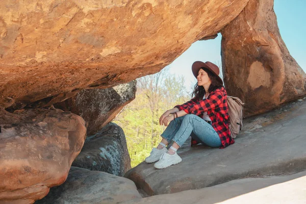 Kotlu ve şapkalı mutlu kadın kayanın orada oturuyor.