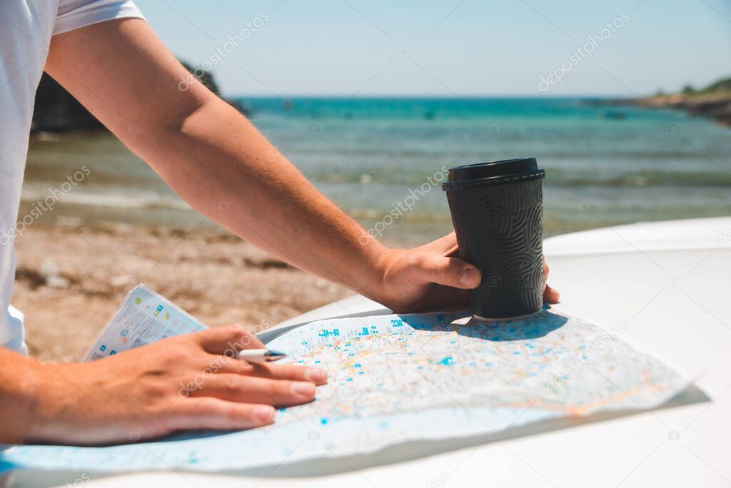 man hands on map at car hood holding coffee cup summer time sea vacation