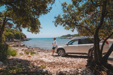 Yaz Denizi Sahili Özgürlük Seyahat Konsepti 'nde beyaz SUV arabasının yanındaki adam.