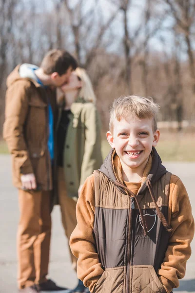 前で微笑む小さな男の子 背景に両親にキス 秋の季節 — ストック写真