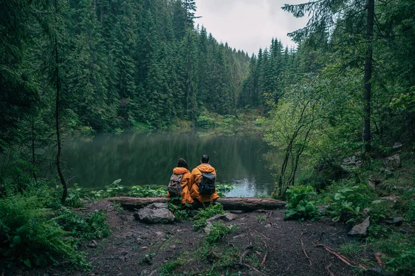 Para Turystów Żółtym Płaszczu Przeciwdeszczowym Patrząc Górskie Jezioro Backpackers — Zdjęcie stockowe