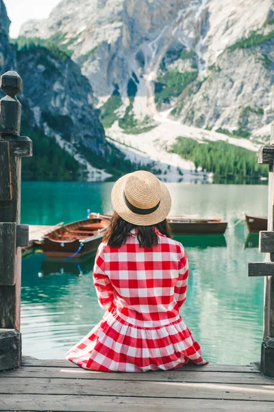 Mujer en vestido rojo sentado en escaleras de madera mirando el lago en las montañas — Foto de Stock