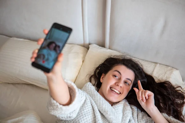Young happy woman taking selfie story laying down in bed — Stockfoto