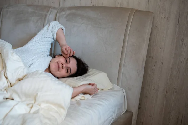 Morgon i sängen kvinna vaknar liggande i sängen med vita lakan — Stockfoto