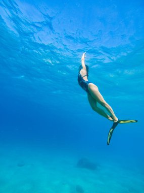 Şnorkel maskesi ve yüzgeçleriyle suyun altında yüzen güzel bir kadın.
