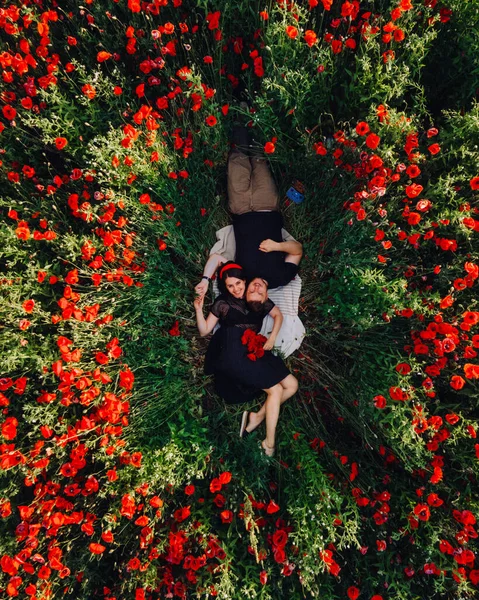 可愛いカップルがポピー畑の真ん中に寝そべってる オーバーヘッドビュー デートのコンセプト — ストック写真