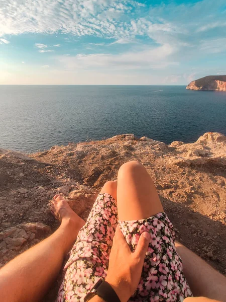 couple sitting on the cliff enjoying view of sunset above the sea no face