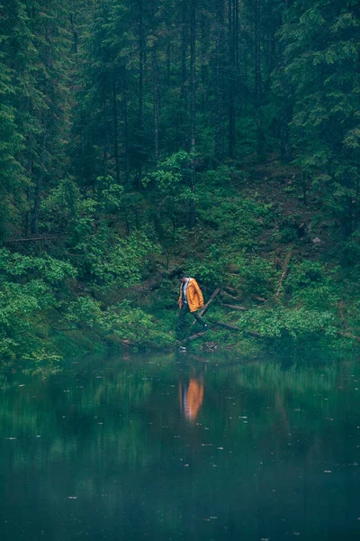 man hiker in yellow raincoat looking at mountain lake traveler concept copy space