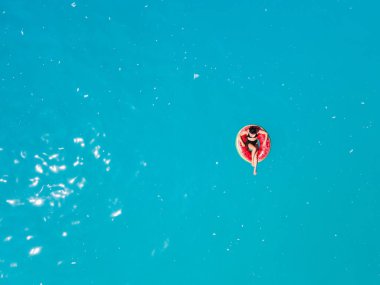 Mavi deniz suyunda güneş banyosu yaparken şişme halkada yüzen kadının tepeden görünüşü