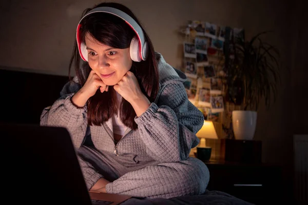 woman with wonder face sitting on the bed looking at laptop screen headset