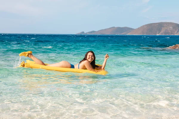 happy woman in blue swimsuit floating on yellow inflatable mattress sea vacation