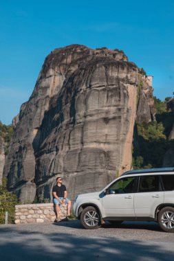 Yunanistan araba yolculuğu konsepti. Cipin yanında duran bir adam meteora manastırına bakıyor.
