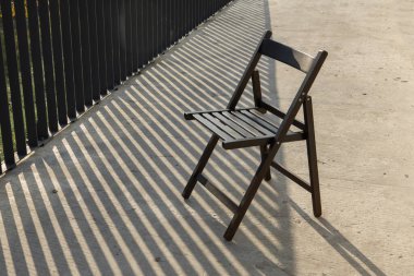 Boş sandalye dışarıda. Sert gölgeler uzayı taklit ediyor.