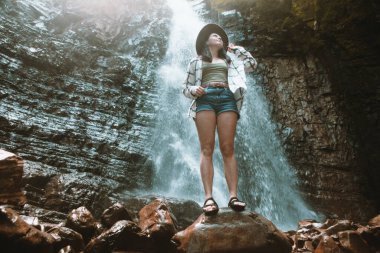 Kahverengi şapkalı kadın şelale yürüyüşünün tadını çıkarıyor.