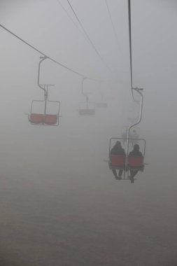 İnsanlar bulutların sisli havasında teleferiğe biniyor.