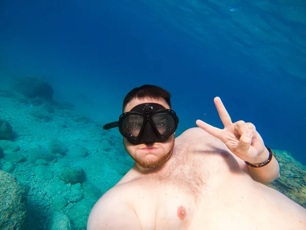 man underwater in scuba mask diving under water taking selfie picture