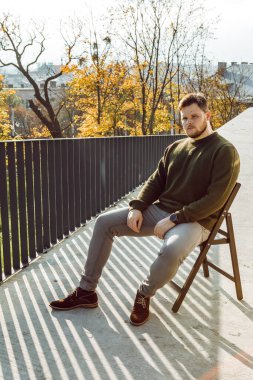 Acımasız yüzlü bir adam açık havada sandalyede oturuyor. Güneşli bir sonbahar günü fotokopi alanı.