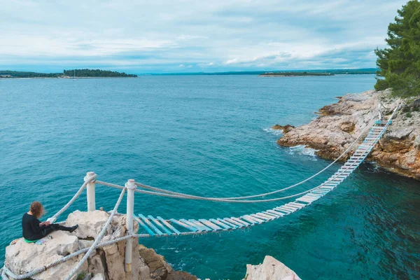 woman sitting at the edge drawing picture of seascape suspension bridge