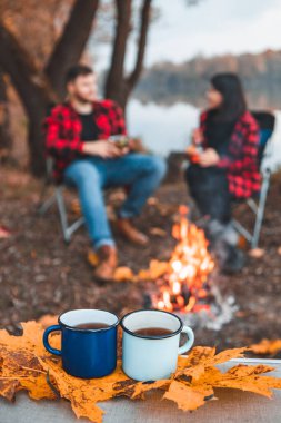 Fotokopi odasının arka planında, ateşin yanında bir adamla çay içen bir kadın.