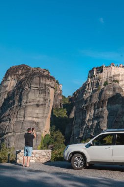 Yunanistan araba yolculuğu konsepti. Cipin yanında duran bir adam meteora manastırına bakıyor.