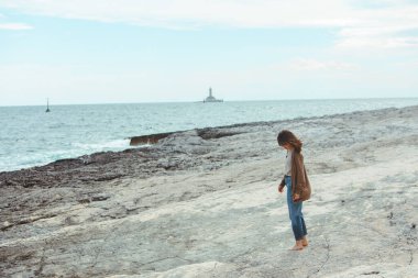 arka planda ıslak kot deniz feneri kayalık deniz plajı tarafından yürüyen kadın. rüzgarlı hava. yaz tatili. kaygısız kavram