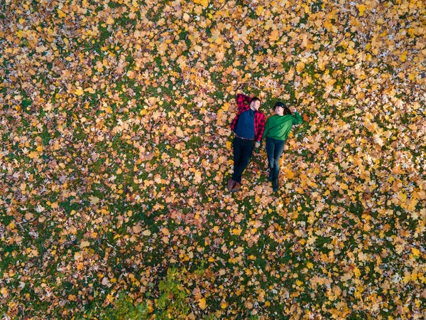 overhead view of woman with man laying down on the ground covered with autumn leaves copy space
