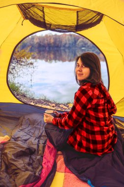 young woman sitting in tent with view of autumn lake camping concept