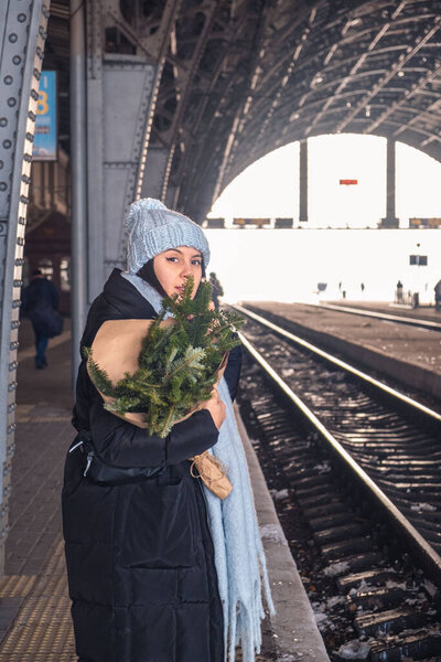 beautiful woman in blue hat at railway station platform with pine tree bouquet copy space