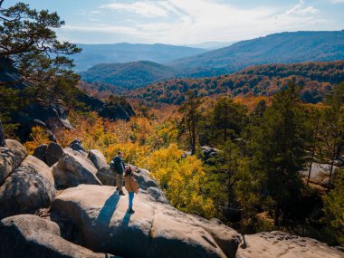 Kayanın tepesinde oturan çift gezgin sonbahar ormanlarının güzel manzarasıyla fotokopi uzayı.