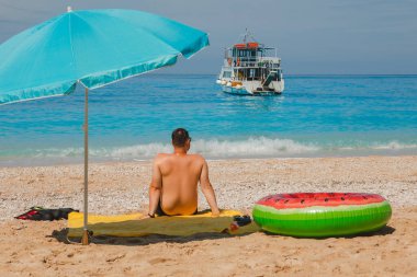 Deniz kıyısında güneşli bir günde güneşli bir şemsiye Yunan tatil gezisi arka planda küçük bir tekne.