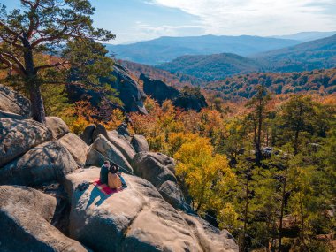 Kayanın tepesinde oturan çift gezgin sonbahar ormanlarının güzel manzarasıyla fotokopi uzayı.