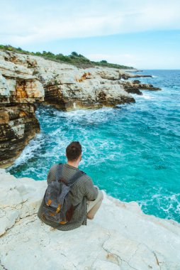 sırt çantası ile adam şehir manzarası zevk uçurumun üzerinde oturan. yaz tatili