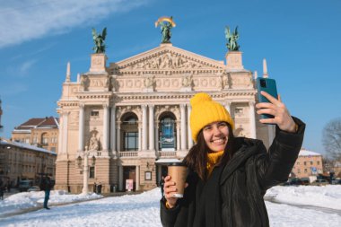 Kadın gezgin, opera binası Ukrayna 'nın önünde selfie çekmek için kahve içiyor.