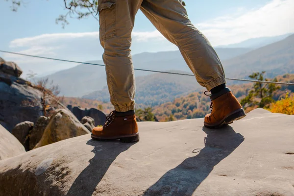 hiking concept men legs in boots on the rock autumn season