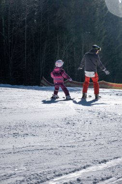Kayak pistinde genç bir aile kızına kayak öğretiyor.