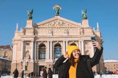 Gülümseyen kadın, Lviv City Ukrayna 'nın opera binasının önünde selfie çekiyor.