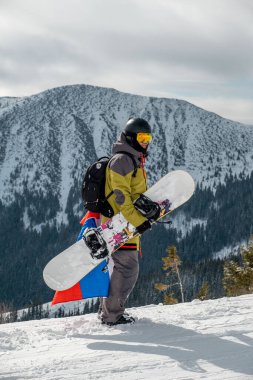 Slovakya bayrağı taşıyan snowboardcu kayak merkezinin yamacında arka planda güzel dağlar var.