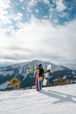 Slovakya bayrağı taşıyan snowboardcu kayak merkezinin yamacında arka planda güzel dağlar var.