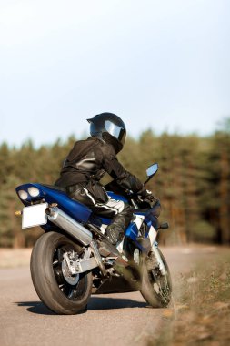 Kasklı ve deri ceketli motosiklet sürücüsü ormanda spor motosikletinin üzerinde oturuyor. Güzel arkaplan, kopyalama alanı için bir yer