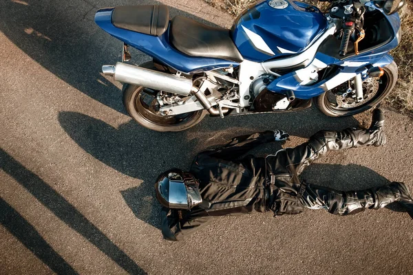 摩托车手身穿皮革防护服 头戴黑色头盔 躺在一辆摩托车附近的沥青路面上 在路上骑黑色自行车的人 从上面看 — 图库照片
