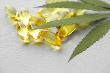 CBD yağ hapları. Beyaz zemin üzerinde şeffaf CBD Cannabidiol kapsülü ve kenevir yaprakları grubu. Organik beslenme takviyeleri kavramı