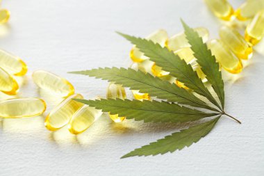 CBD yağ hapları. Beyaz zemin üzerinde şeffaf CBD Cannabidiol kapsülü ve kenevir yaprakları grubu. Organik beslenme takviyeleri kavramı