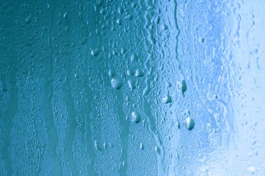 Doğal su buharlaşmasının mavi arka planı, yüksek hava ve nemli pencere camları, büyük damlalar. Toplanıyor ve aşağı akıyor
