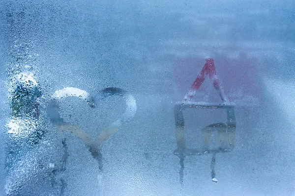 Close-up on love heart and home condensation lettering against sweaty window glass. Hand draws a heart and a house on a foggy window