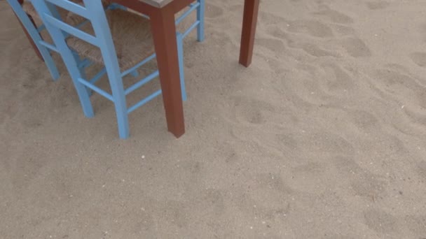 구름낀 저녁에는 그리스의 모래가 해변에서 파란색 의자들이 널빤지로 탁자를 매달아 — 비디오