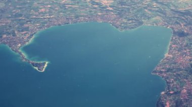 Çerçevenin sağına bakarak gölün üzerinden uçarak git. Yolcu engelsiz bir şekilde Garda Gölü manzaralı. Yüksek irtifada seyreden bir uçakta küçük evleri var..