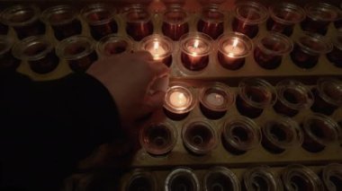 Katolik kilisesindeki bir tezgahta mum yakmak. Aydınlık ve yakılmamış beyaz adak mumları, karanlık bir arka plana karşı sakin alevleri olan metal bir kapta Hıristiyan duası için kullanılıyor..