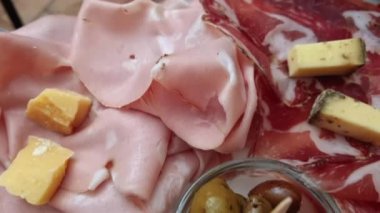 Platter of various cold meats and cheese on a wooden tray. Smoked boneless ham and other assorted slices snacks served as an appetizer at a local delicatessen in Bologna, Italy. 